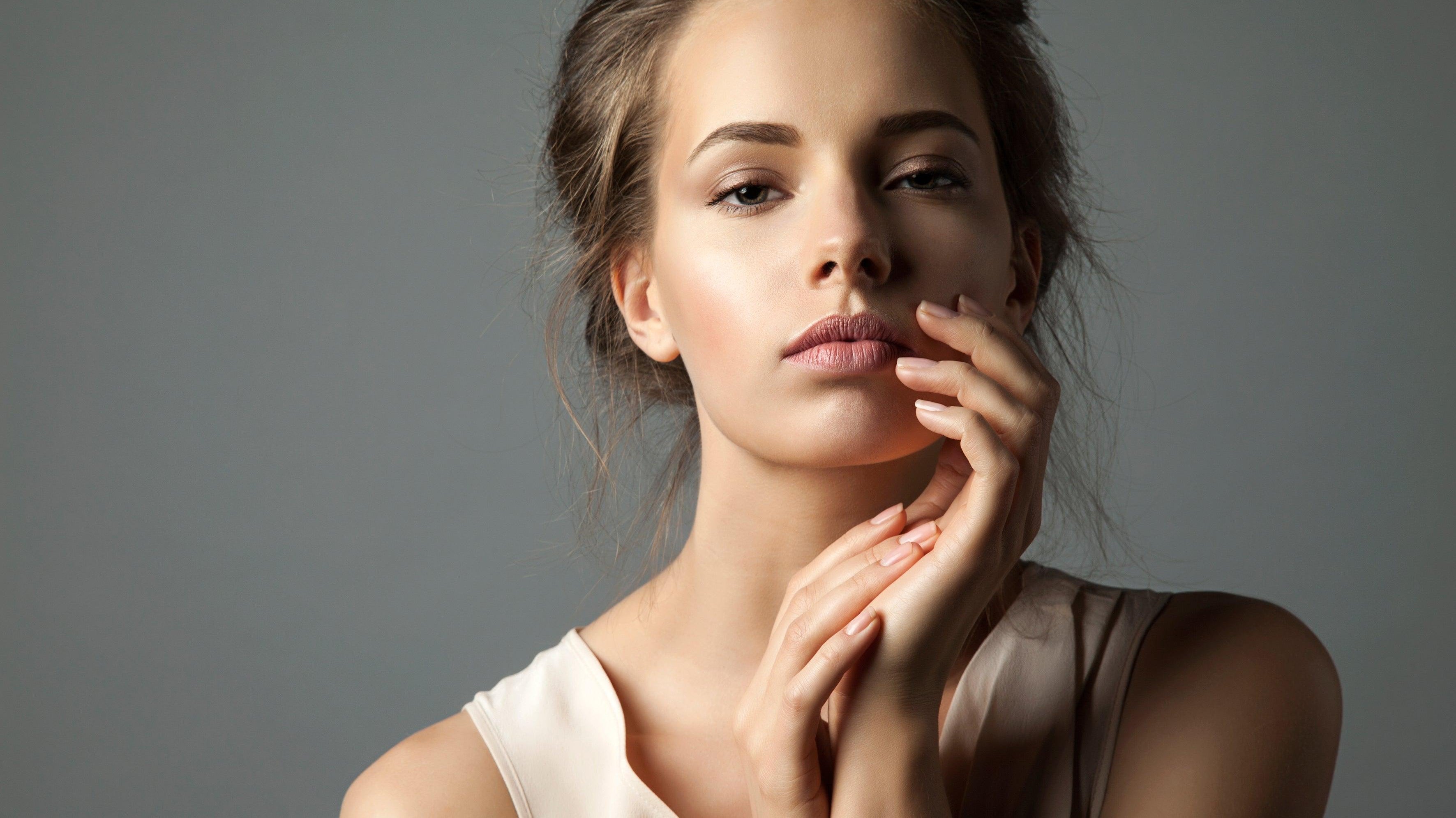 Woman with glowing skin and natural makeup posing against a neutral background