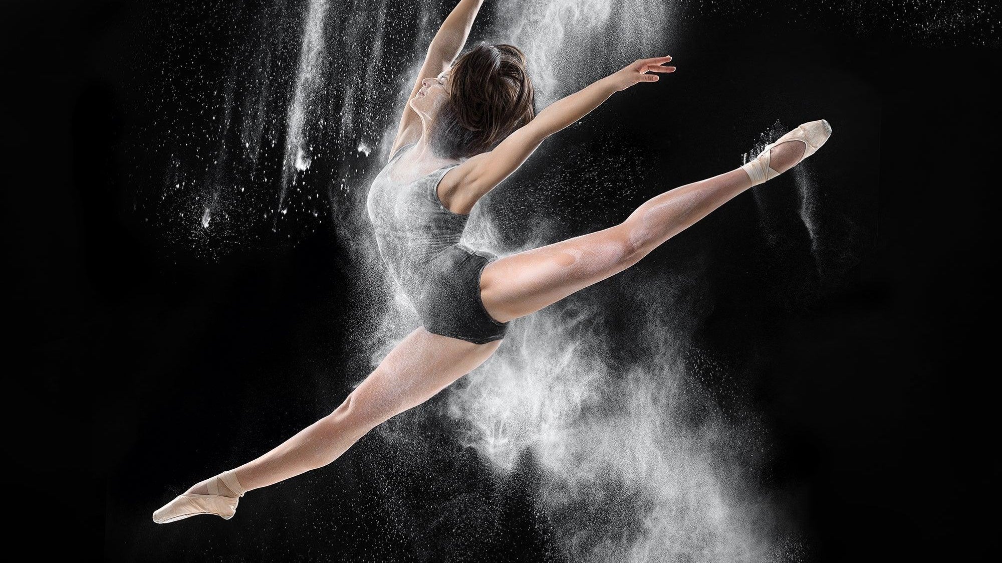Ballet dancer in mid-leap with powder, expressive dance pose on black background