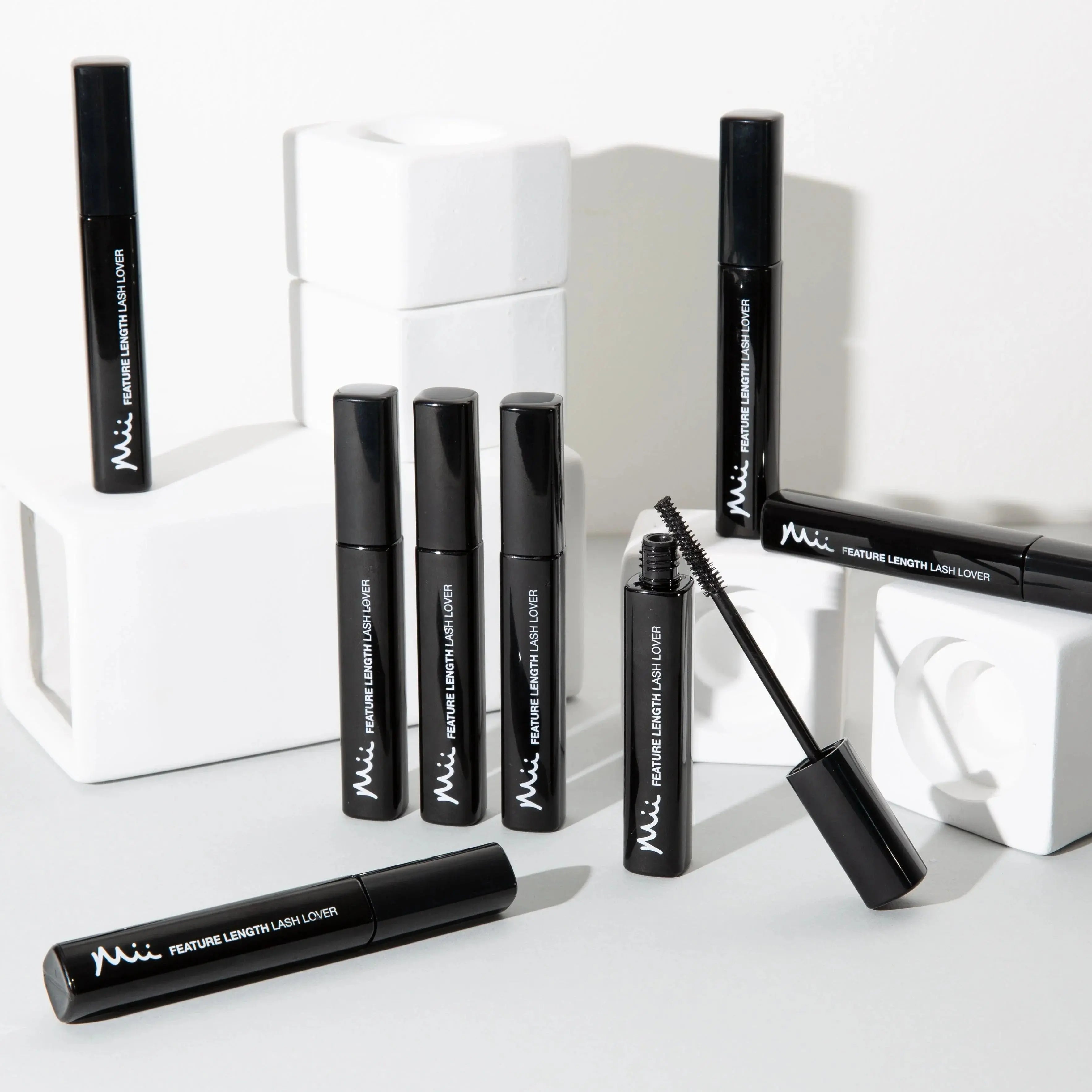 Mii Feature Length Lash Lover mascara tubes arranged on white blocks with one open showing brush