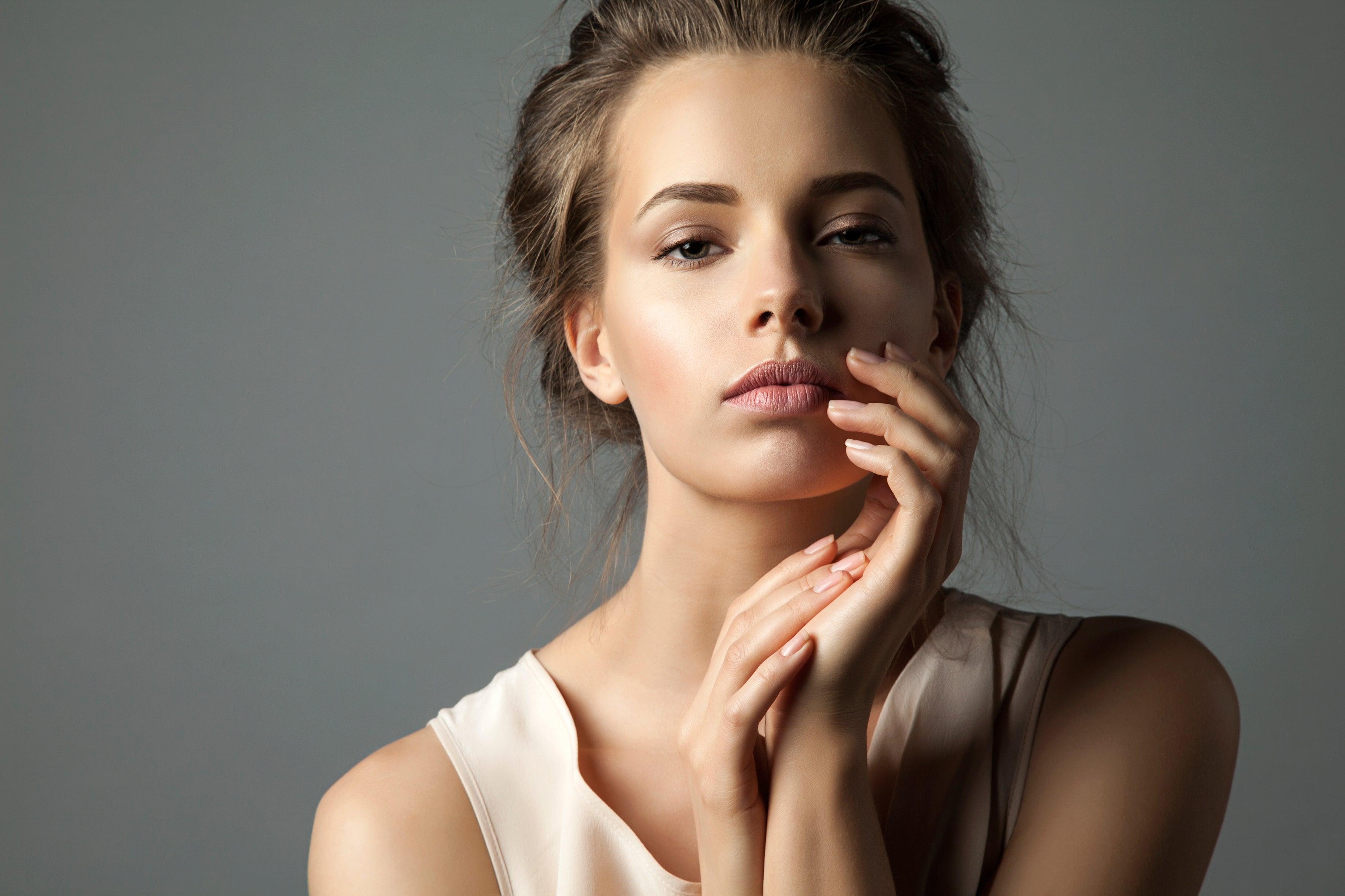 Woman with glowing skin and natural makeup posing against a neutral background