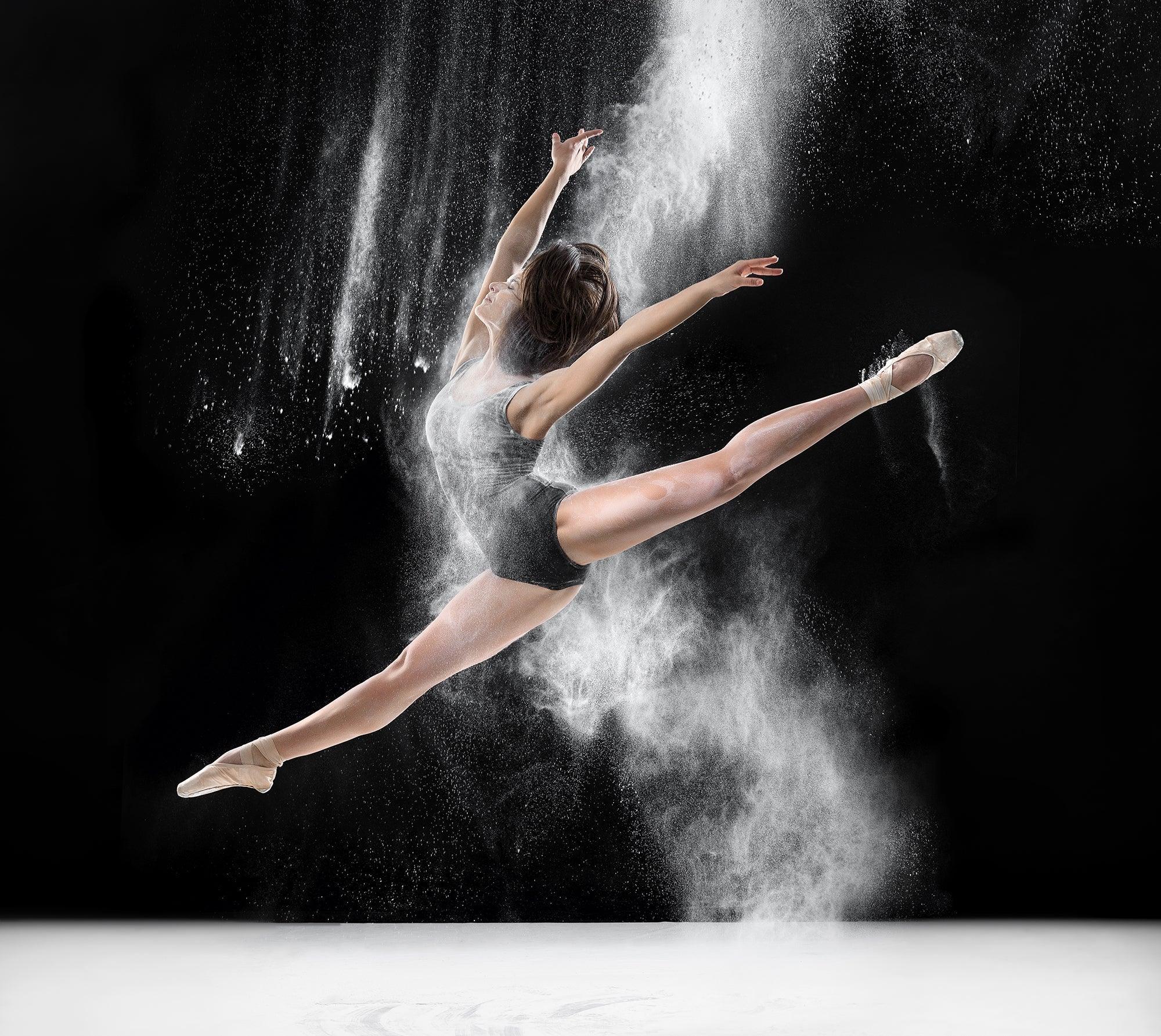 Ballet dancer in mid-leap with powder, expressive dance pose on black background