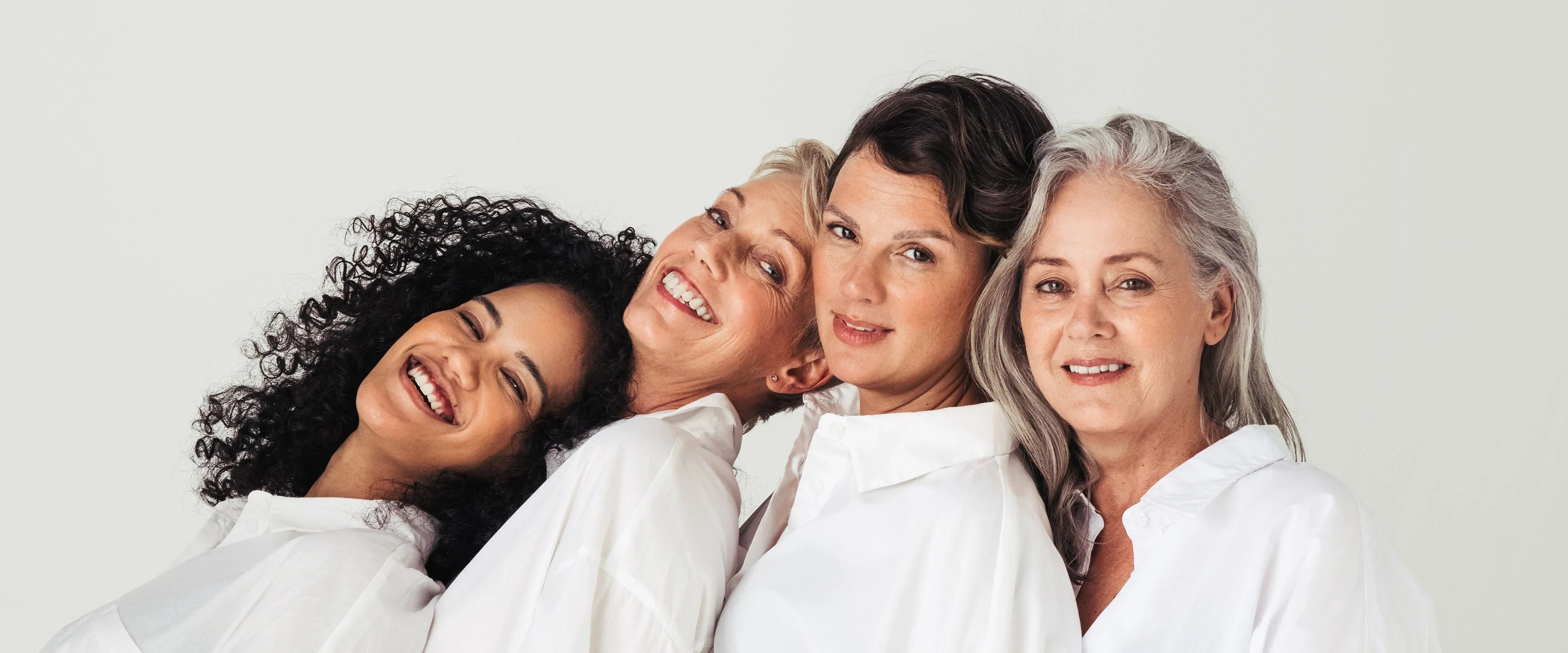 Four diverse women of varying ages smiling in white shirts against a neutral background